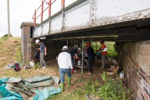 Volunteers stir the paint prior to applying it to the cleaned up structural pieces, with the help of Graham Peacock.