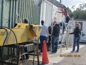 Nationwide Building Society volunteers cleaning the flaking and faded paint off the containers near the main entrance to the railway. Note how pale the container on the right looks, the biscuit paint has faded quite a lot. Photo: Grahame Every